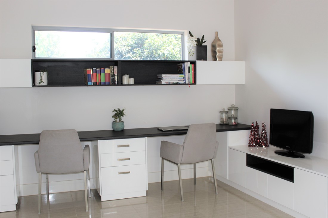 Photograph of the built study, showing the black open shelf holding books above a dark benchtop and white drawers