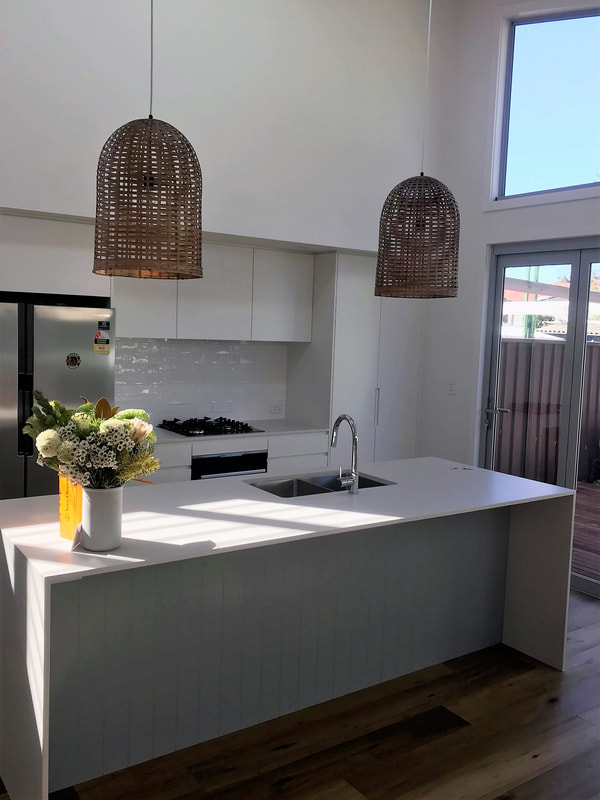 Photograph of a finished white kitchen with a vee-groove panelled island and woven pendant lights