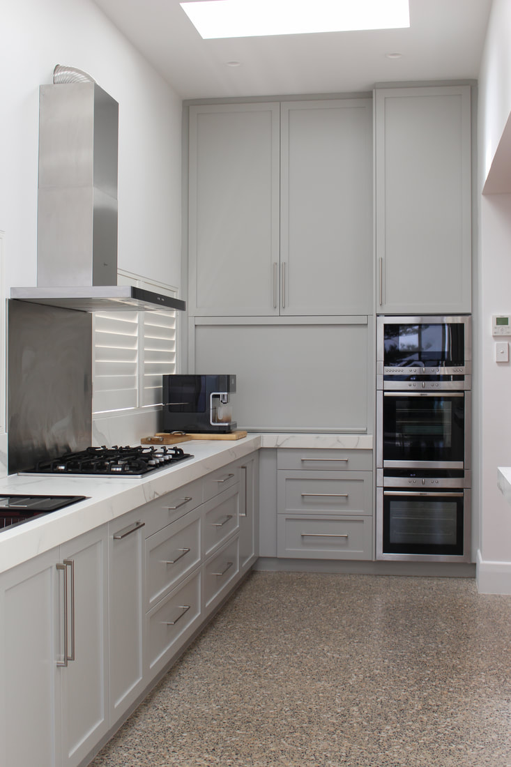 Photograph of the finished grey shaker kitchen with a marble benchtop, stainless wall ovens and a terrazzo floor