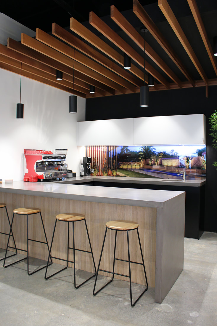 Photograph of the finished cafe, showing the timber battened ceiling, concrete benchtop and timber-clad bar with stools
